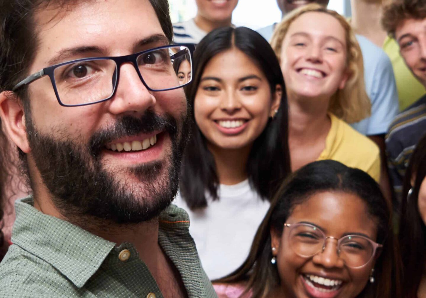 Happy vertical selfie of young group of students taking a photo with their male teacher in the classroom. Classmates from different countries, looking at camera with big smiles.